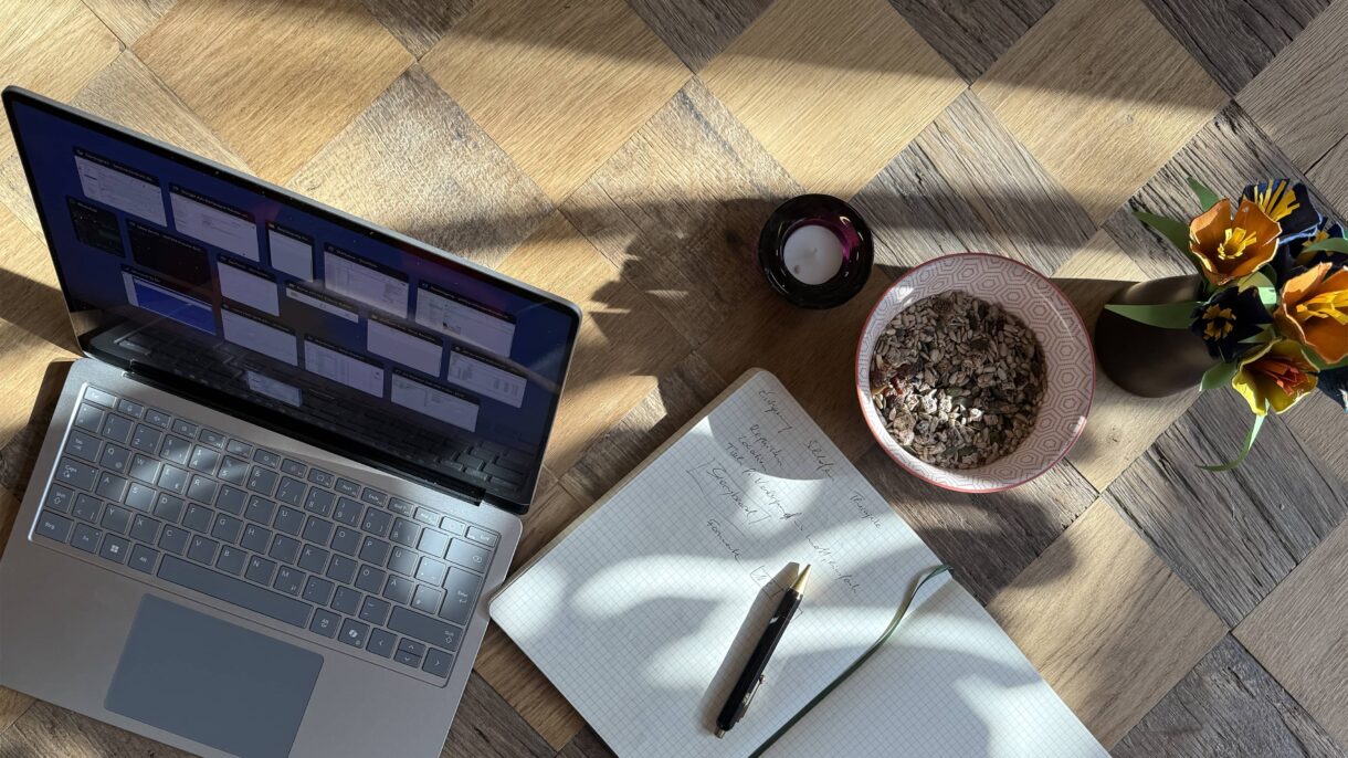 Laptop auf Holztisch mit Notizbuch und Stift nebenbei