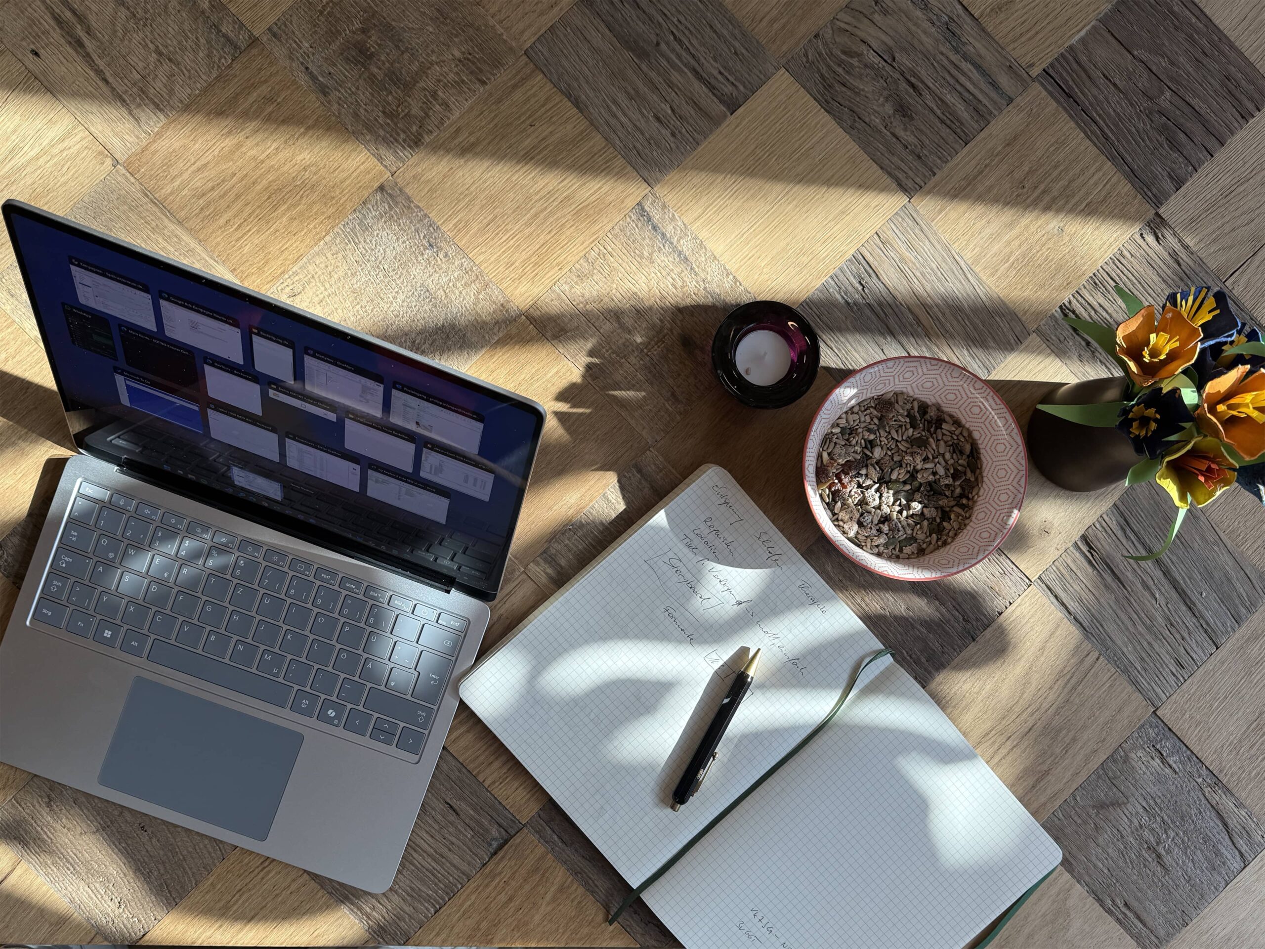 Laptop auf Holztisch mit Notizbuch und Stift nebenbei