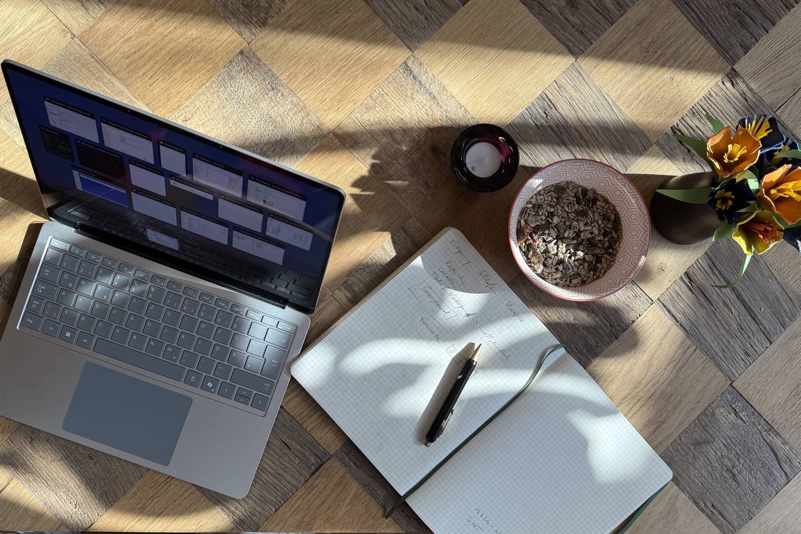 Laptop auf Holztisch mit Notizbuch und Stift nebenbei